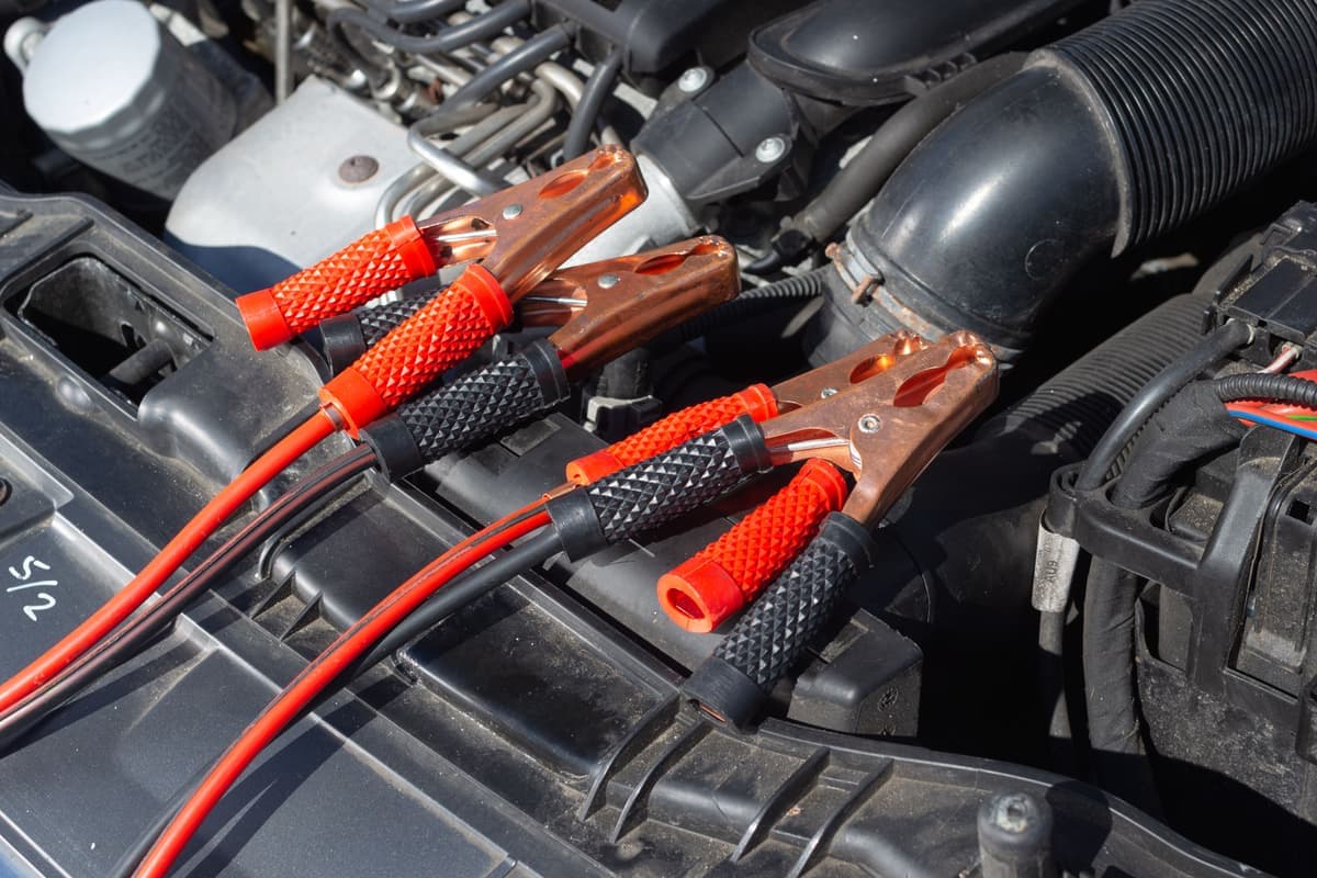A close-up of a car engine bay with battery clamps