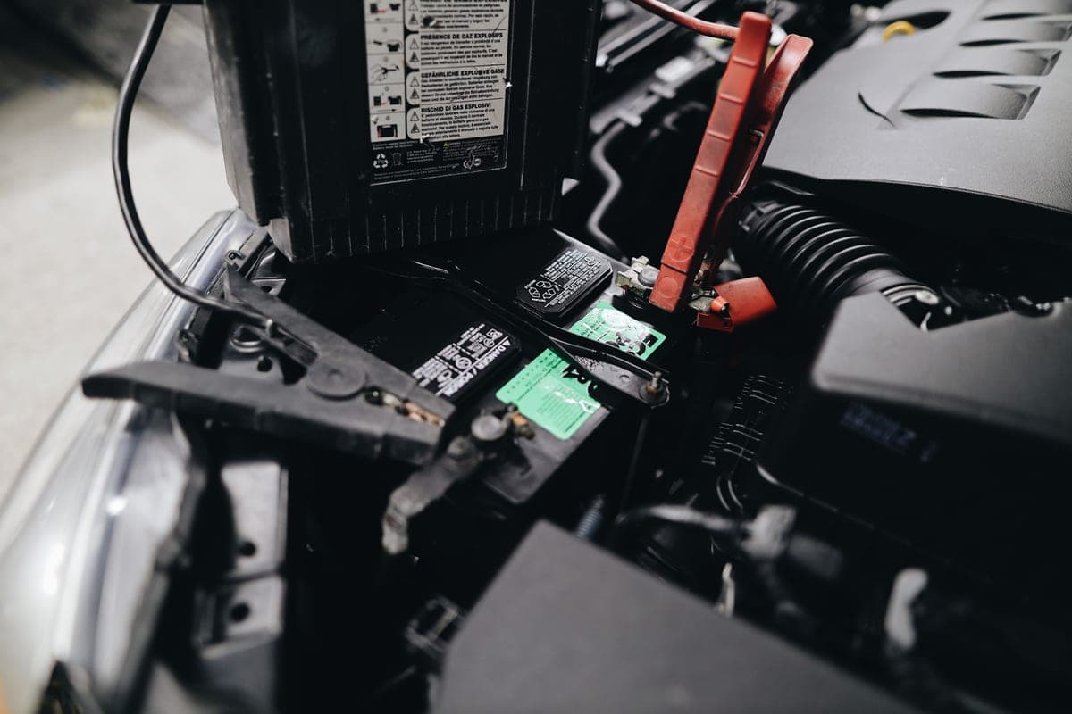 A compact lithium jump starter beside a car battery in an engine bay